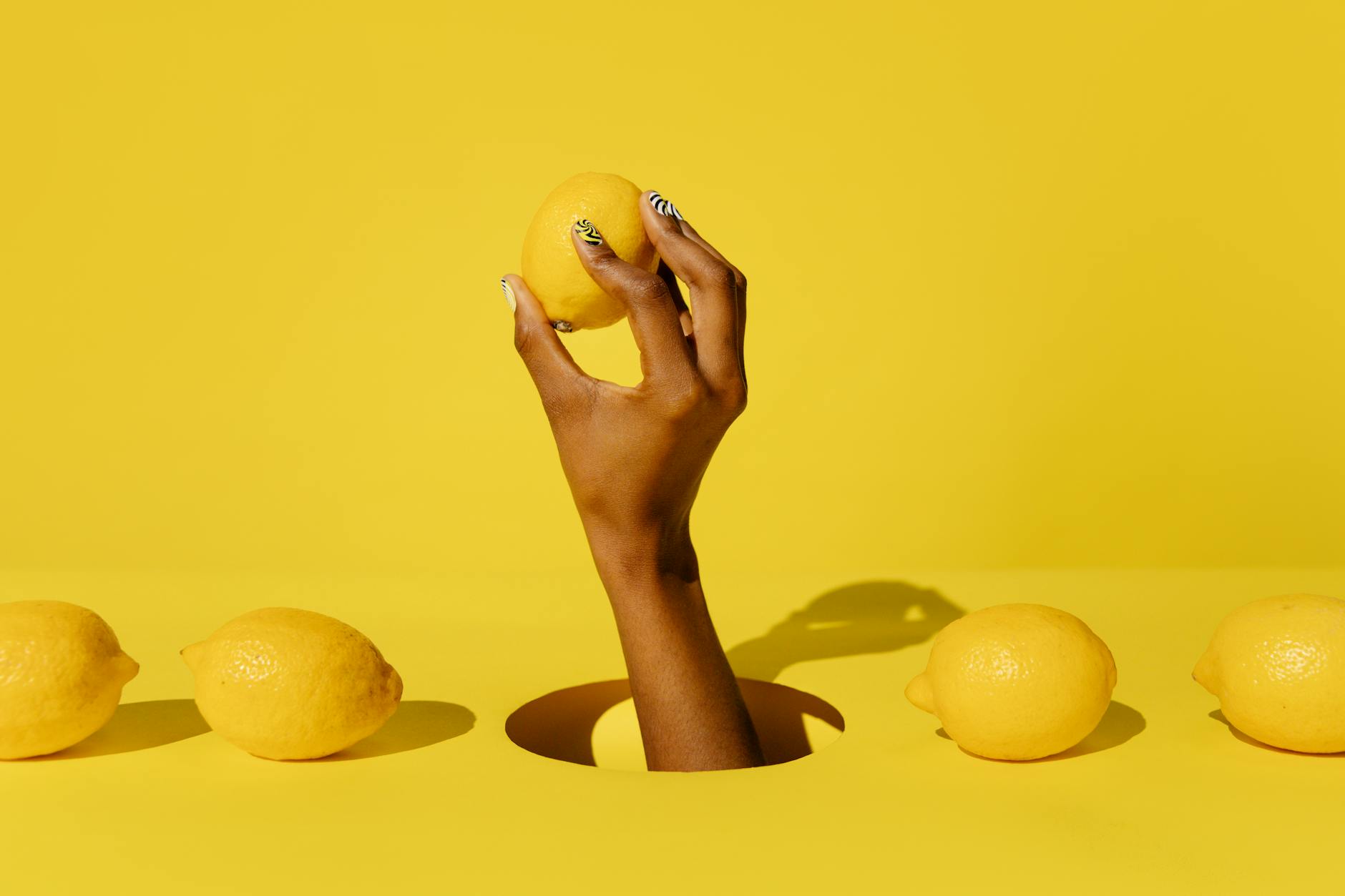 A hand holding a lemon against a vivid yellow background, representing freshness and renewal in intimate connection