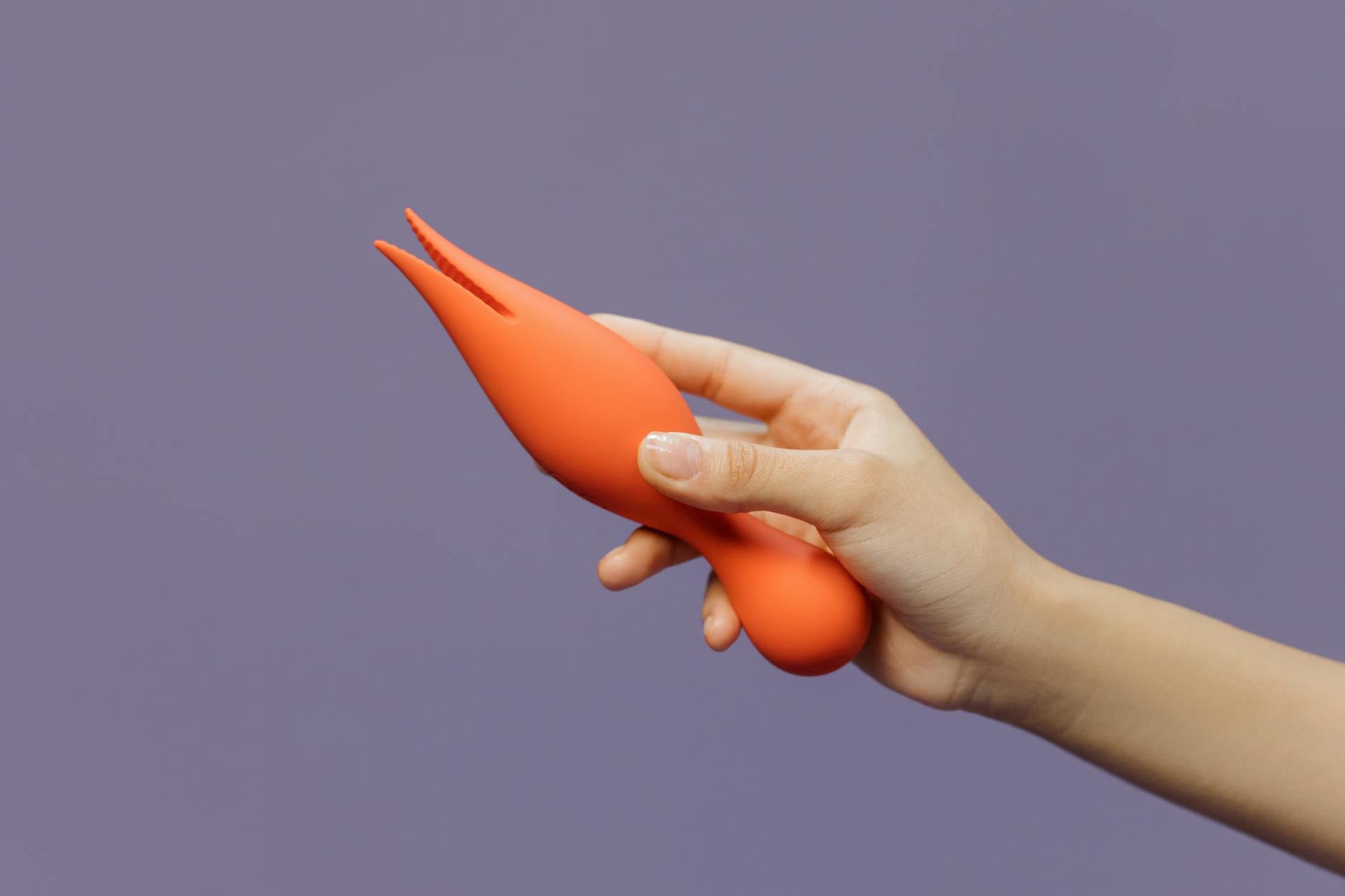 A close-up of a hand holding a lemon-colored vibrator against a purple backdrop