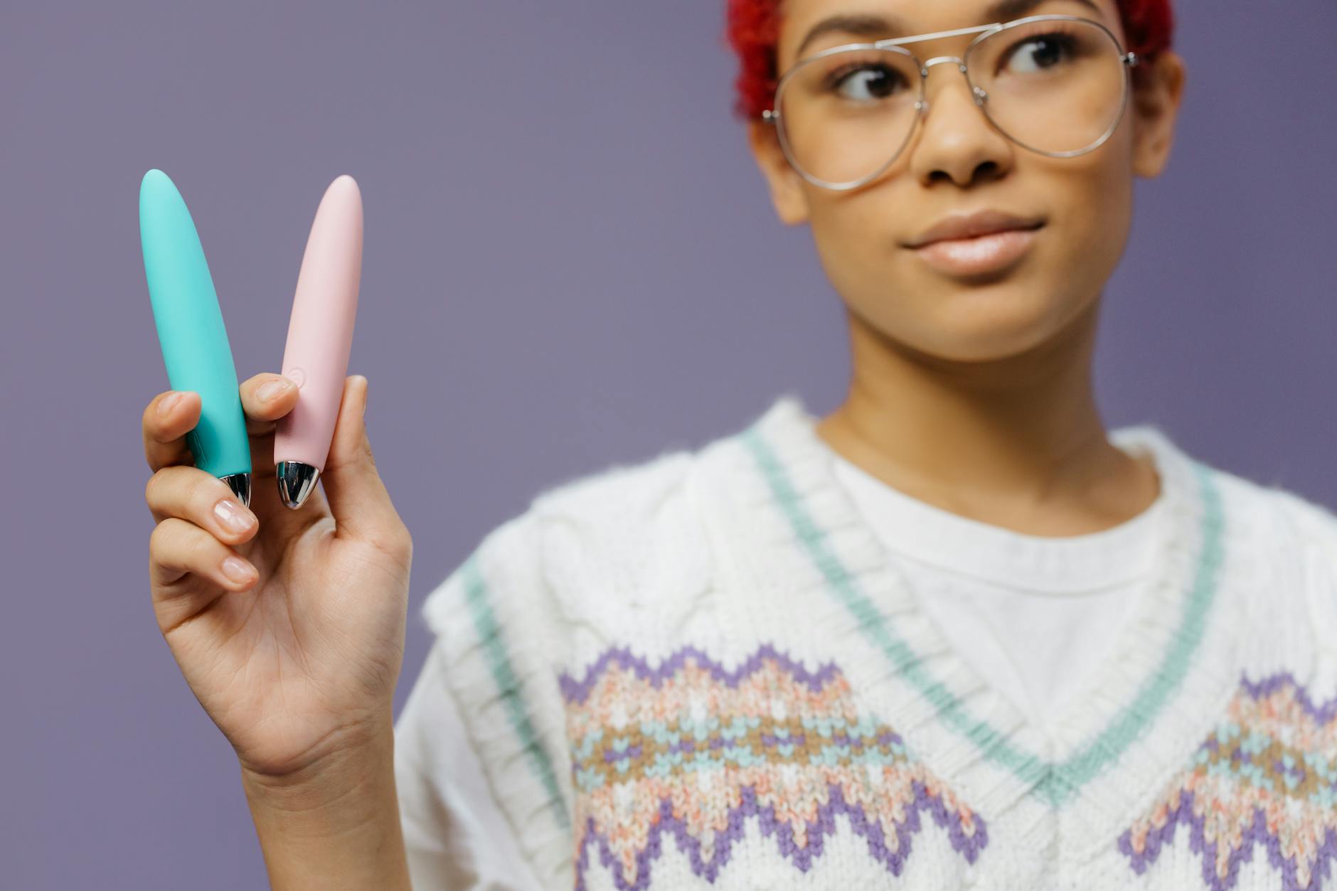 A woman holds two colorful vibrators against a purple background, showcasing options for extended arousal sessions
